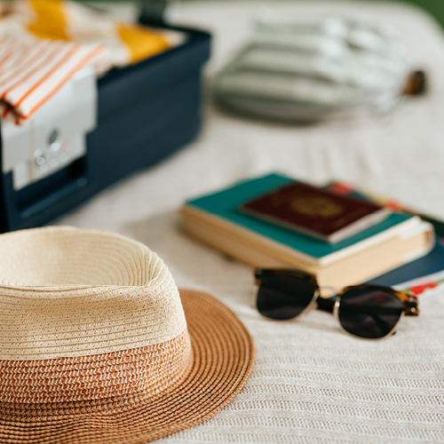 suitcase with clothes, a hat, books, passport and sunglasses on a bed