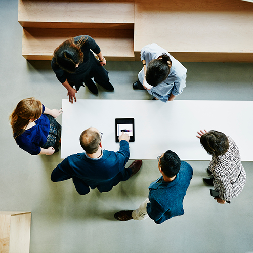a team of people gathered around a table looking at a tablet