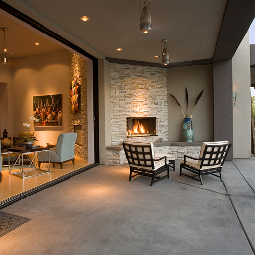 Elevated aesthetic outdoor patio with fireplace, furniture and full wall window view into the home