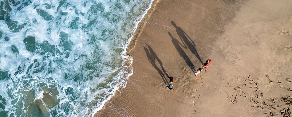 Drone view of a family walking along beach by the ocean
