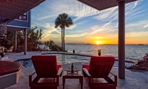 Beautiful view of reclined lounger chairs with table wine glasses and wine bottle by swimming pool and Tampa Bay at sunset