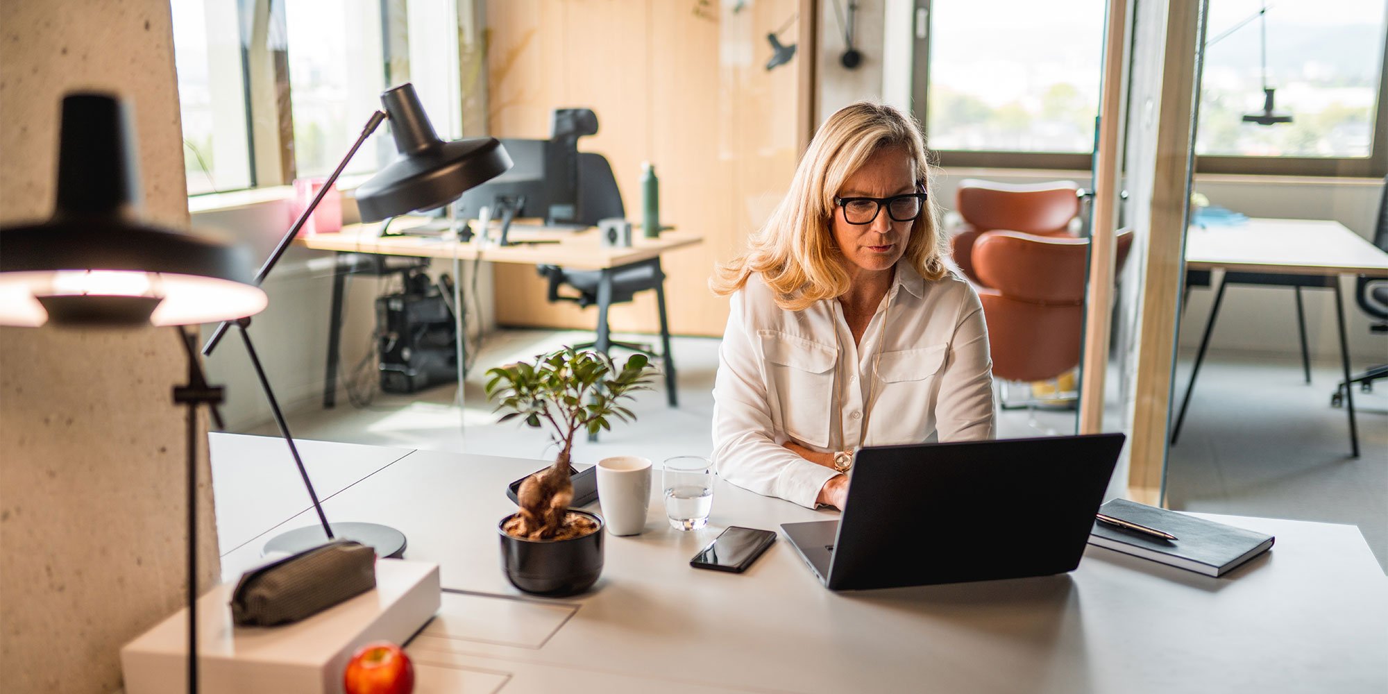 Woman in glasses sitting looking at laptop in office space